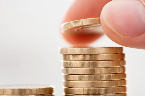 Hand som staplar mynt, symboliserar ekonomisk ersättning från a-kassan och inkomstförsäkringen.
