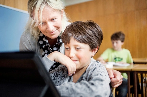 En lärare hjälper en elev med en iPad i klassrummet.