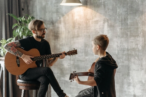En lärare spelar gitarr tillsammans med en elev, vilket symboliserar kreativ undervisning och den trygghet som Lärarnas a-kassa erbjuder för lärare i deras pedagogiska arbete.