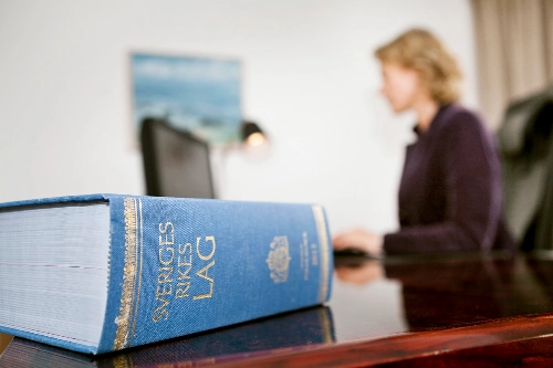 En svensk lagbok ligger på ett bord med en person i bakgrunden, vilket symboliserar att Lärarnas a-kassa måste förhålla sig inom lagens ramar.
