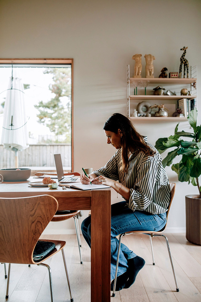 Lärare som sitter vid sitt köksbord och antecknar samtidigt som hon tittar på sin laptop.