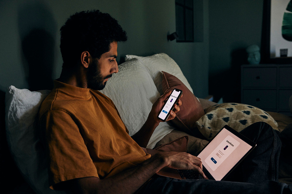 Lärare sitter i soffan och använder bank-id för att logga in på sin laptop.